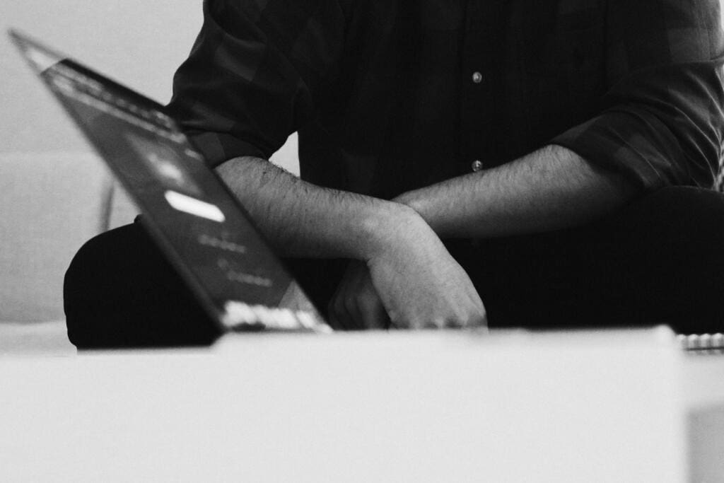 Black and white photo of a person sitting with folded arms beside an open laptop, representing a discussion about building backlinks.